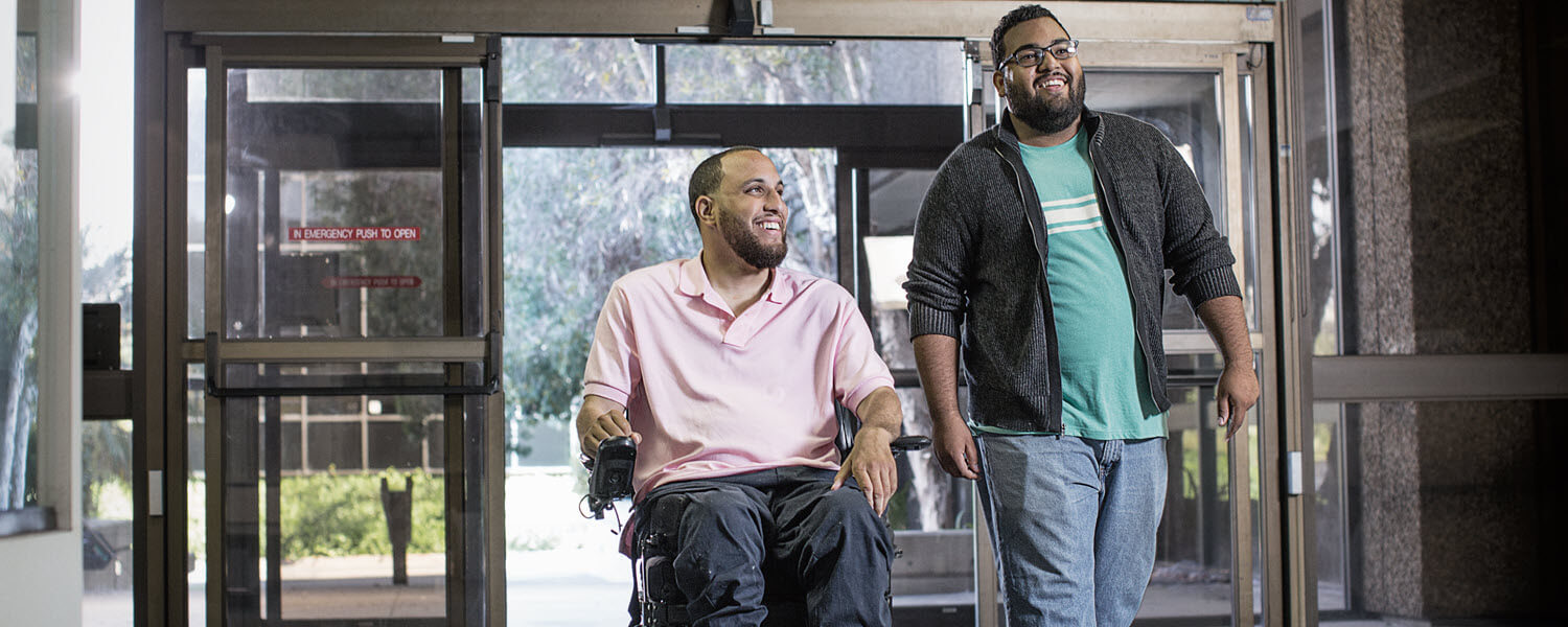 Man in motorized wheelchair and friend entering a building